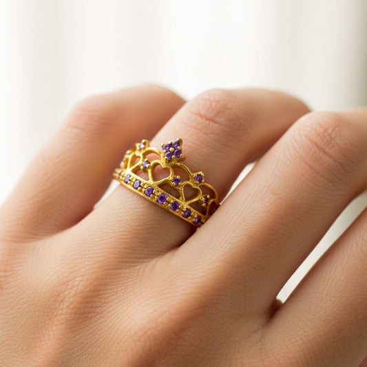 Mano de mujer usando un anillo con forma de corona en el centro en oro amarillo de 18 quilates con cristales de color morado de Joyería Caracas.
