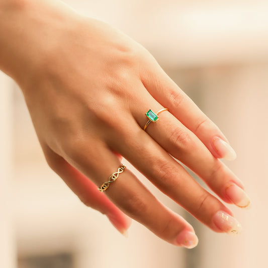 Mano de mujer con anillo en oro amarillo de 18 quilates con piedra preciosa de esmeralda natural en corte rectangular.