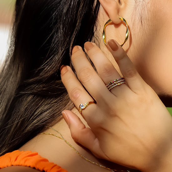 Mano de mujer usando un anillo de compromiso en oro amarillo de 18 quilates con cristal redondo en el centro de color blanco y alrededor de él de Joyería Caracas.