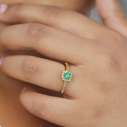 Mano de mujer usando un anillo con forma cuadrada en el centro en oro amarillo de 18 quilates, Esmeralda redonda de color verde en el centro y Diamantes de color blanco alrededor de él y laterales de Joyería Caracas.