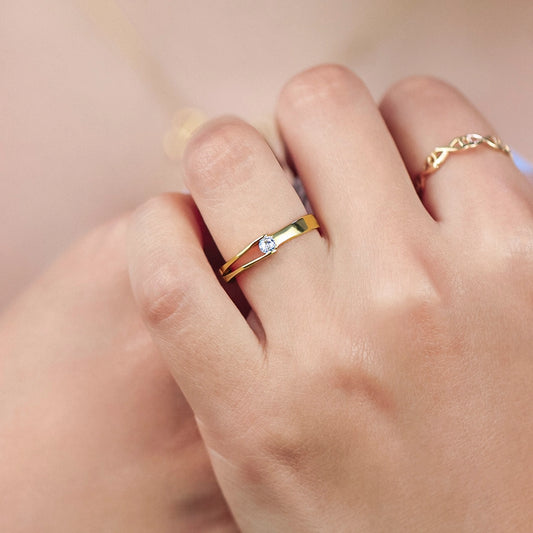 Mano de mujer usando un anillo con abertura en el aro en forma de vértice en oro amarillo de 18 quilates con cristal en el centro de color blanco de Joyería Caracas.