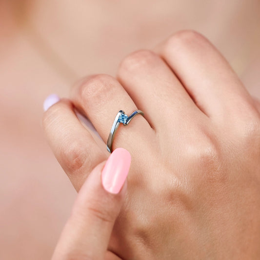 Mano de mujer usando un anillo en oro blanco de 18 quilates en forma de onda con un cristal de color azul celeste en el centro de Joyería Caracas.