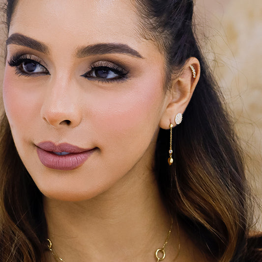 Oreja de mujer con arete largo con forma de corazón en la punta en oro amarillo de 18 quilates y cristal de color blanco.