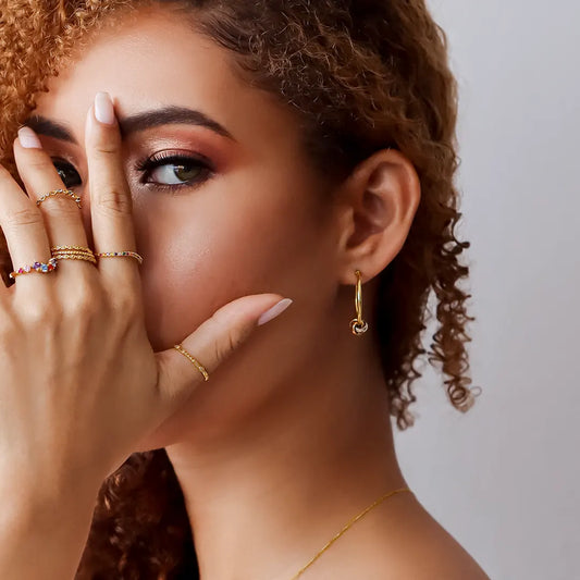 Oreja de mujer usando aretes de tubo con una esfera en forma de nudo en oro amarillo, blanco y rosa de 18 quilates de Joyería Caracas.