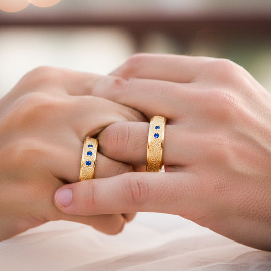 Manos de una pareja usando unas argollas en oro amarillo de 18 quilates facetadas con cristales azules de Joyería Caracas.