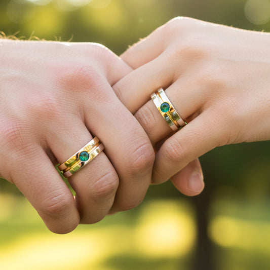 Manos de una pareja usando unas argollas de matrimonio en oro blanco y amarillo de 18 quilates con cristal verde de Joyería Caracas.