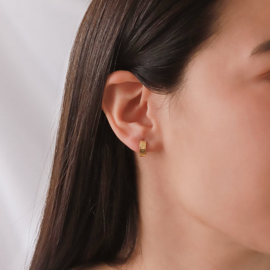Oreja de mujer usando candongas con textura en líneas horizontales en oro amarillo de 18 quilates de Joyería Caracas.