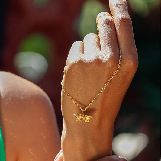Mano de mujer con cadena y dije en forma de mariposa en oro amarillo de 18 quilates con cristales de distintos colores, hecho en Joyería Caracas.