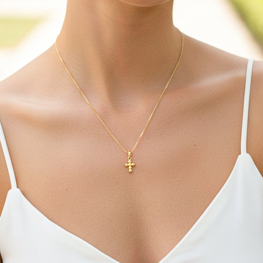 Cuello de modelo usando una cadena con un dije en forma de cruz de esfera en oro amarillo de 18 quilates de Joyería Caracas.