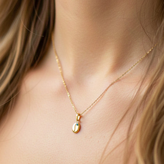Cuello de modelo usando una cadena con un dije en forma de grano de café en oro amarillo de 18 quilates con Esmeralda de Joyería Caracas.