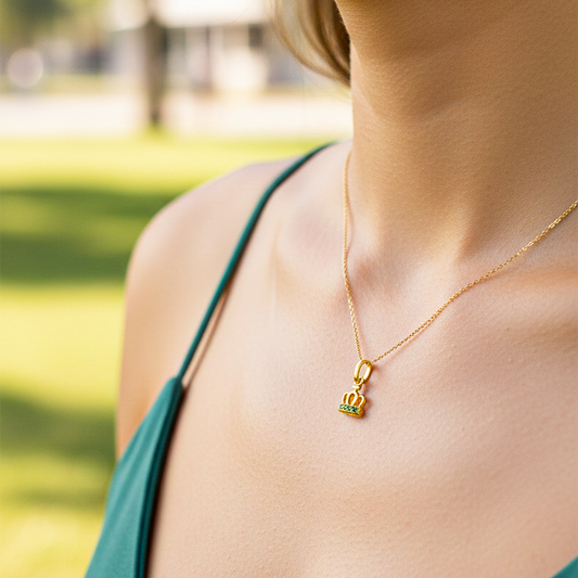 Cuello de modelo usando una cadena con un dije en forma de corona en oro amarillo de 18 quilates con cristales verdes de Joyería Caracas.