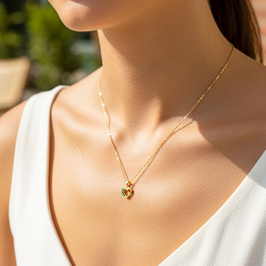 Cuello de modelo usando una cadena con un dije en forma de corazón en oro amarillo de 18 quilates con cristales verdes de Joyería Caracas.