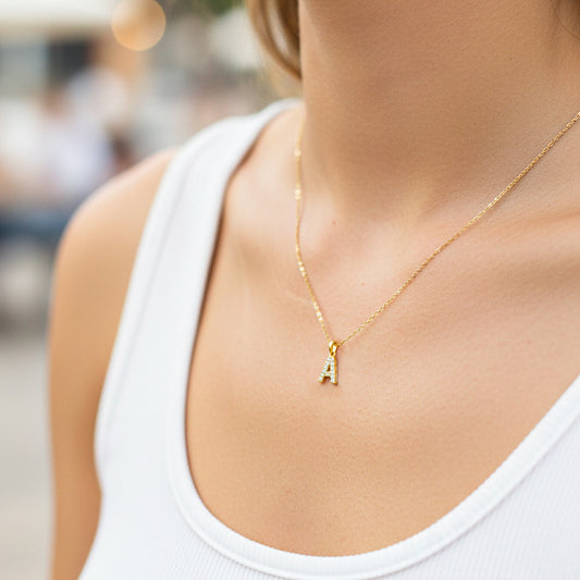 Cuello de modelo usando una cadena con un dije de la letra A en oro amarillo de 18 quilates con cristales de Joyería Caracas.