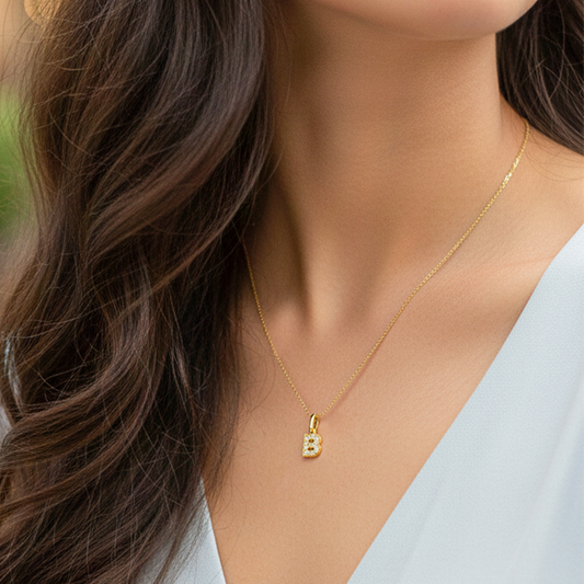 Cuello de modelo usando una cadena con un dije en forma de la letra B en oro amarillo de 18 quilates con cristales de Joyería Caracas.