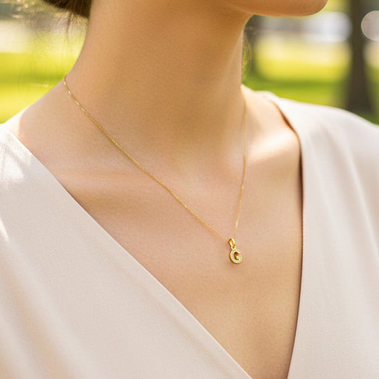 Cuello de modelo usando una cadena con un dije de la letra G en oro amarillo de 18 quilates con cristales de Joyería Caracas.