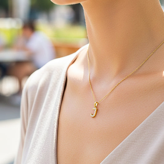 Cuello de modelo usando una cadena con un dije de la letra J en oro amarillo de 18 quilates con cristales de Joyería Caracas.