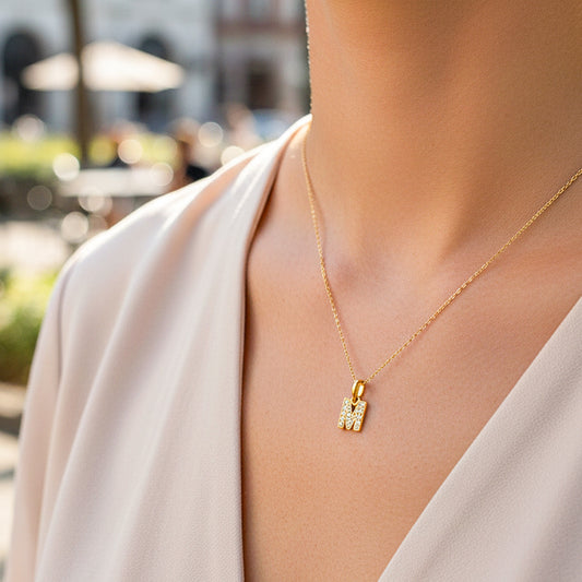 Cuello de modelo usando una cadena con un dije de la letra M en oro amarillo de 18 quilates con cristales de Joyería Caracas.