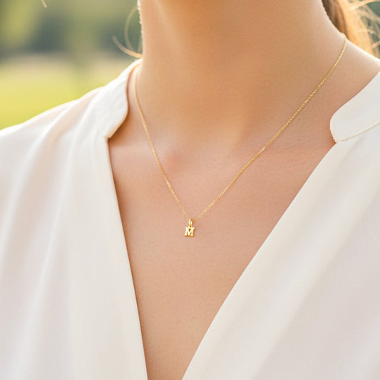 Cuello de modelo usando una cadena con un dije en forma de letra M en oro amarillo de 18 quilates de Joyería Caracas.