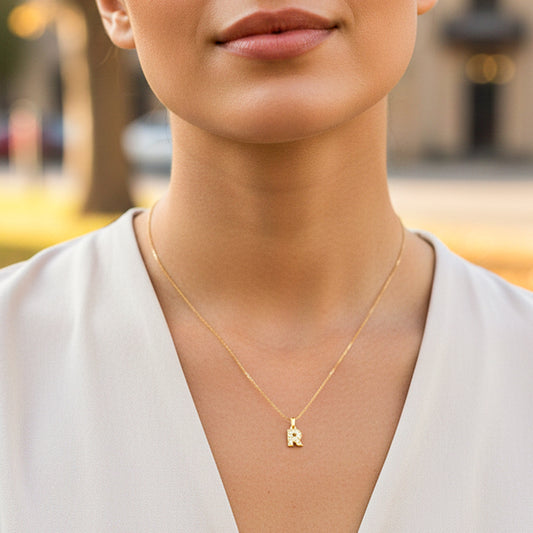 Cuello de modelo usando una cadena con un dije en forma de la letra R en oro amarillo de 18 quilates con cristales de Joyería Caracas.