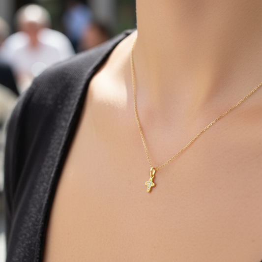 Cuello de modelo usando una cadena con un dije en forma de mini cruz en oro amarillo de 18 quilates con cristales de Joyería Caracas.
