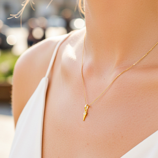 Cuello de modelo usando una cadena con un dije en forma de mini raqueta de tenis en oro amarillo de 18 quilates con cristales de Joyería Caracas.