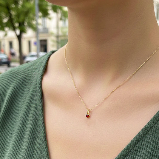 Cuello de modelo usando una cadena con un dije en forma de corazón en oro amarillo de 18 quilates con cristal rojo de Joyería Caracas.