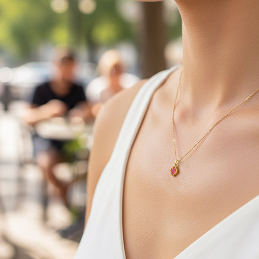 Cuello de mujer usando una cadena con dije en forma de trébol en oro amarillo de 18 quilates y piedra en forma de trébol en color rojo de Joyería Caracas.
