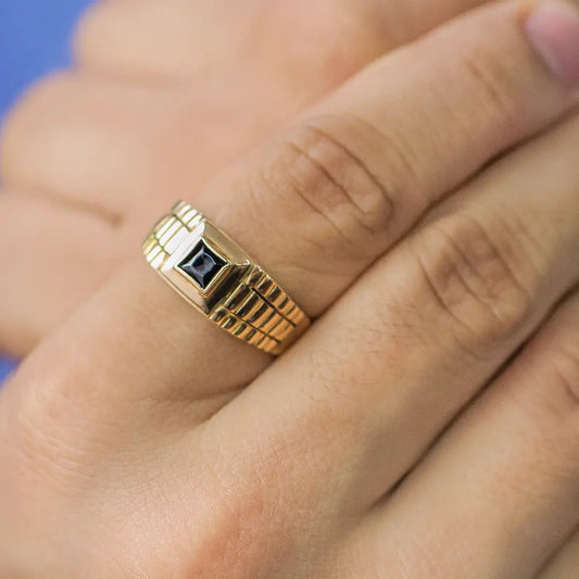Mano de hombre con anillo Armis en oro amarillo de 18 quilates con cristal de color negro en el centro, hecho en Joyería Caracas.