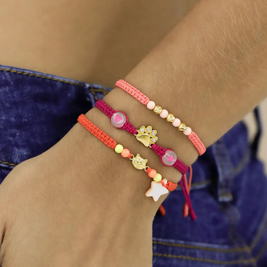 Mano de mujer con pulsera tejida en hilo fucsia oscuro, bisutería y dije en forma de huella de perro en oro amarillo de 18 quilates con cristales de color blanco, hecho en Joyería Caracas.