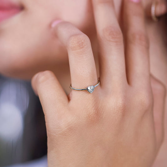 Mano de mujer usando anillo con corazón en el centro en oro blanco de 18 quilates y diamante en forma de corazón en color blanco, hecho en Joyería Caracas.
