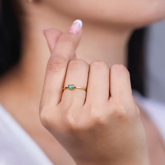 Mano de mujer con anillo en oro amarillo de 18 quilates con piedra esmeralda en forma de corazón de color verde, hecho en Joyería Caracas.