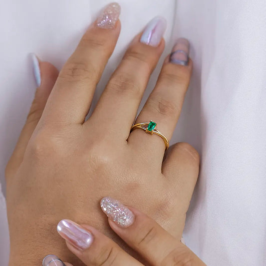 Mano de mujer con anillo en oro amarillo de 18 quilates y esmeralda en corte baguette, hecho en Joyería Caracas.