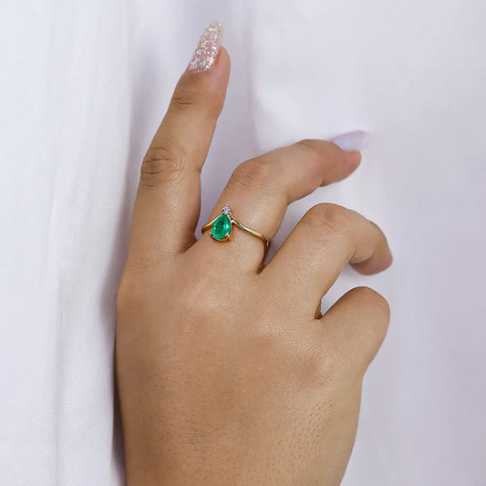 Mano de mujer con anillo en oro amarillo de 18 quilates, esmeralda en forma de gota y cristal de color blanco, hecho en Joyería Caracas.