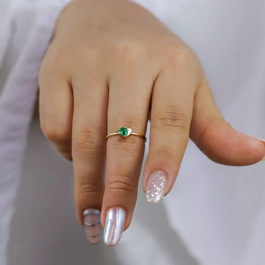 Mano de mujer con anillo en forma de corazón en oro amarillo de 18 quilates y esmeralda en forma de gota, hecho en Joyería Caracas.