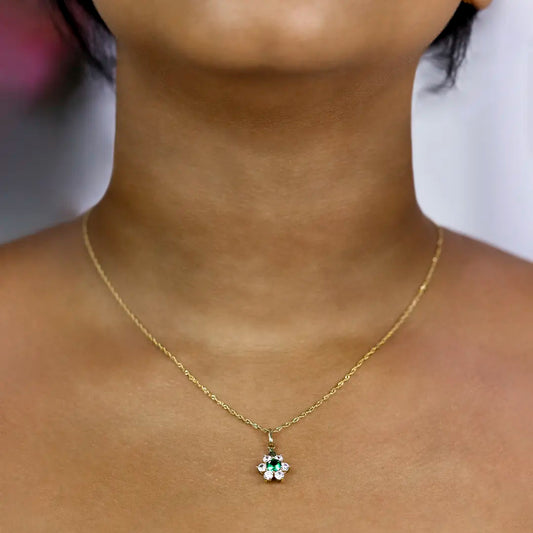 Cuello de mujer con dije en forma de flor en oro amarillo de 18 quilates, un cristal de color verde en el centro y 6 cristales de color blanco como pétalos, hechos en Joyería Caracas.