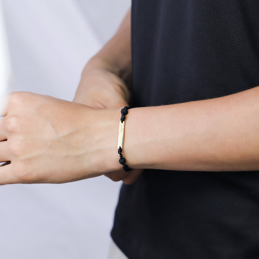 Mano de hombre con pulsera tejida en hilo negro y placa lisa para grabado laser en oro amarillo de 18 quilates, hecho en Joyería Caracas.