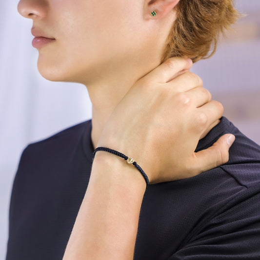 Mano de hombre con pulsera tejida en hilo negro con dije San Benito pasante de 7.0mm en oro amarillo de 18 quilates, hecho en Joyería Caracas.