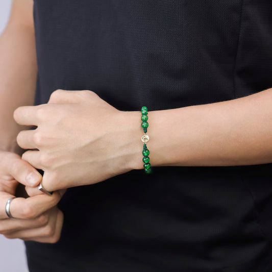 Mano de hombre con pulsera tejida en hilo, con accesorios de color verde y dije de San Benito en oro amarillo de 18 quilates, hecho en Joyería Caracas.