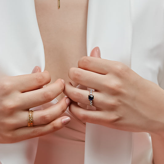 Mano de mujer con anillo en oro amarillo de 18 quilates, con cristales de color blanco y cristal de color azul en forma cuadrada, hecho en Joyería Caracas.