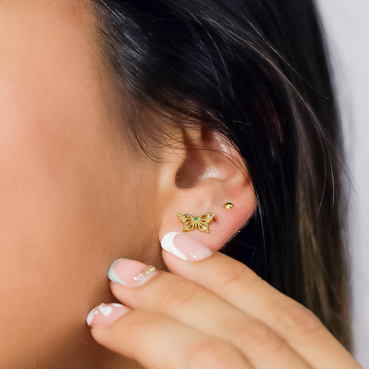 Oreja de mujer con topito en forma de mariposa en oro amarillo de 18 quilates con un cristal de color verde y 4 cristales de color blanco, hechos en Joyería Caracas.
