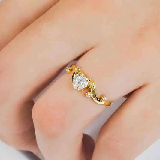 Mano de mujer con anillo en oro amarillo de 18 quilates con cristal en forma de corazón en el centro de color blanco y alrededor circulares, hecho en Joyería Caracas.