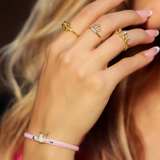 Mano de mujer con pulsera tejida en hilo rosa con blanco coreano con dije de corona y 2 esferas en oro amarillo de 18 quilates, hecho en Joyería Caracas.
