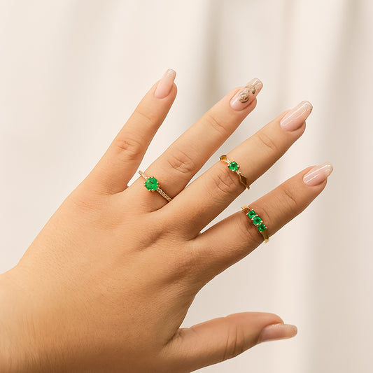 Mano de mujer con anillo en oro amarillo de 18 quilates con una forma en su aro triangular en ambos lados, con Esmeralda natural en el centro de color verde y 2 Diamantes a cada lado de color blanco, fabricado en Joyería Caracas.