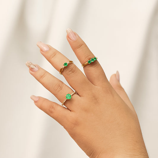 Mano de mujer con anillo en oro amarillo de 18 quilates con Esmeralda de color verde en el centro y Diamantes de color blanco en los laterales, siendo así una pieza única fabricada en Joyería Caracas.