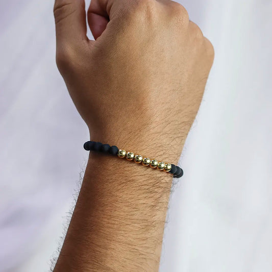 Mano de hombre con pulsera tejida en hilo negro con accesorios en neopreno negro y esferas en oro amarillo de 18 quilates, hecho en Joyería Caracas.