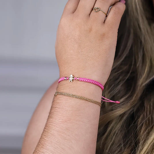 Mano de mujer con pulsera tejida en hilo rosa con accesorios en color rosa y dije de Niña en oro amarillo de 18 quilates.