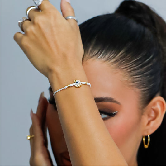 Mano de mujer con pulsera tejida en hilo blanco, bisutería y esferas lisas en oro amarillo de 18 quilates, hecho en Joyería Caracas.