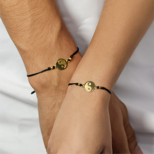 Mano de mujer y hombre con pulsera tejida en hilo negro coreano, dije en forma de Yin y Yang y 2 esferas en oro amarillo de 18 quilates, hecho en Joyería Caracas.