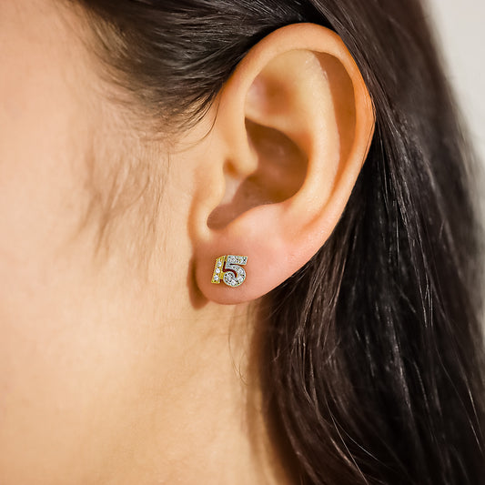 Oreja de mujer con topito con el número 15 en oro amarillo y blanco de 18 quilates con cristales de color blanco, hechos en Joyería Caracas.