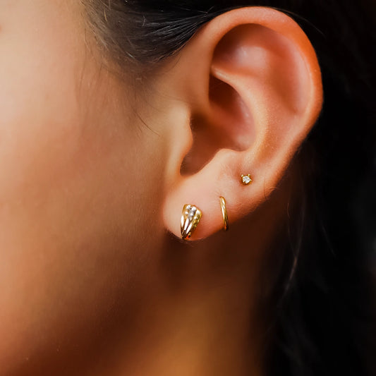 Oreja de mujer usando un topito en forma de abanico en oro amarillo, blanco y rosa de 18 quilates en Joyería Caracas.